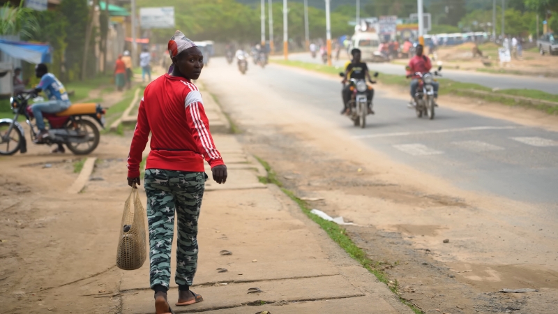 A Local Person Walking Along a Street in Ethiopia, with Motorcycles Passing by In the Background