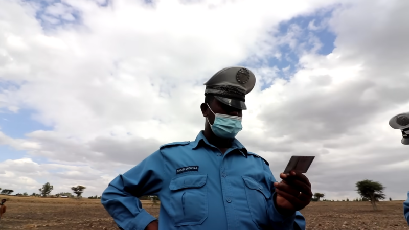 A Police Officer in Ethiopia, Wearing a Mask and Uniform, Inspecting a Document Under a Cloudy Sky